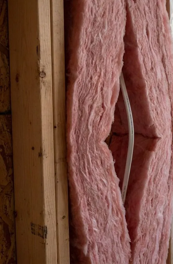 A pink fibreglass batt peeled open through its thickness, with a white electrical cable running inside the split instead of compressing the batt.